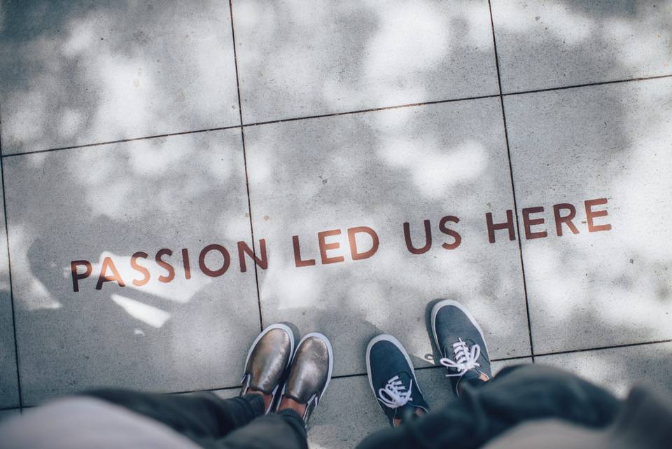 Goal reached? Two pair of feet with sneakers with a sentence on tiles: "Passion let us here"