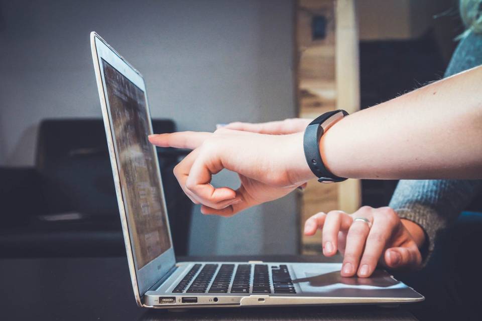 Two hands pointing at laptop screen, one hand on mousepad